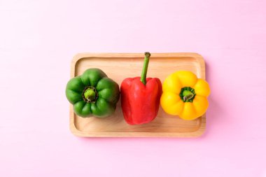 Yeşil, kırmızı ve sarı dolmalık biberler, ahşap tabakta pembe arka planda, üst manzara