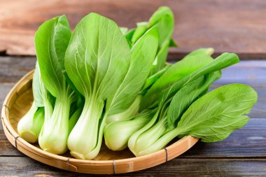 Tahta arka planda bambu sepeti içinde taze Bok Choy veya Pak Choi (Çin lahanası), organik sebzeler