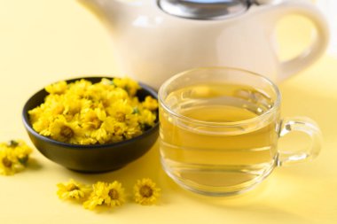 Organik Kasımpatı çiçeği çayı bir fincanda ve çaydanlık sarı arka planda, sağlıklı bitkisel içecek