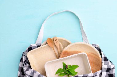 Biyo-çözünebilir, atılabilir, tek kullanımlık ya da çevre dostu kap (tabak, tabak, kase, bardak) kumaş torba içinde pastel renk arka planında, sürdürülebilir konsept