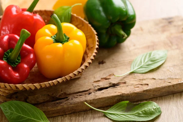 Tahta arka planda bambu sepetinde taze sarı, kırmızı ve yeşil dolma biber, organik sebzeler.
