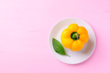 Sarı dolma biber, beyaz tabakta yaprak, pembe arka plan, üst manzara.