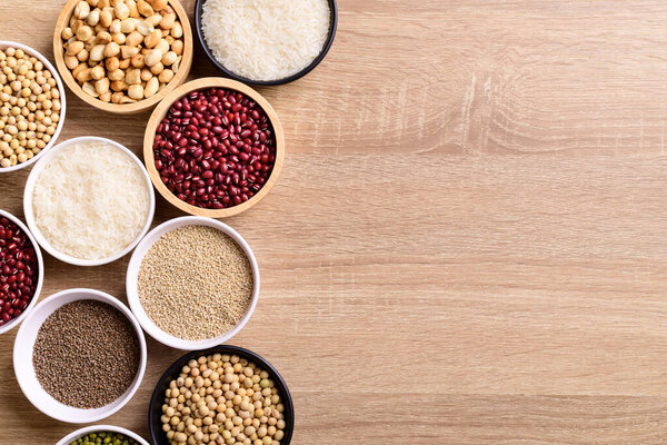 Различные зерновые в миске на деревянном фоне (семена киноа, арахис, семена периллы, соевые бобы, фасоль азуки, рисовое зерно и бобы мунга)