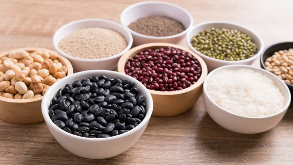 Various cereal grain in a bowl on wooden background (quinoa seeds, black kidney bean, peanut, perilla seeds, soybean, azuki beans, rice grain and mung beans)