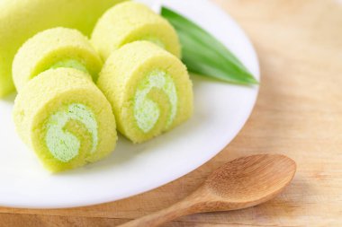 Dilimlenmiş Pandan pastası, beyaz tabakta pandan yaprağı ve tahta masada kaşık.