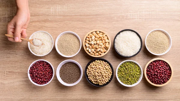 Various cereal grain in a bowl with hand on wooden background (quinoa seeds, peanut, soybean, azuki beans, rice grain and mung beans)