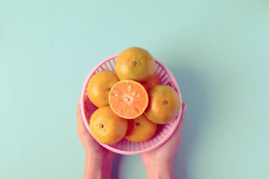 Taze mandalina portakal meyvesi, el ele tutuşturulmuş bir sepetin içinde. Renkli arka planda.