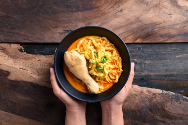 Kuzey Tayland yemekleri (Khao Soi), baharatlı körili şehriye çorbası ve ahşap arka planda elle tutulan tavuk çorbası.