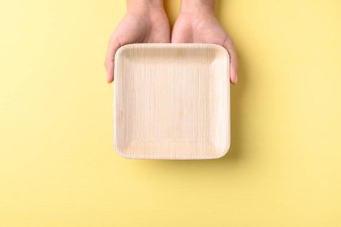 Sarı zemin üzerinde elle tutulan betal palmiye yaprağı (biyolojik olarak ayrıştırılabilir, gübrelenebilir, tek kullanımlık veya çevre dostu plaka), sürdürülebilir konsept