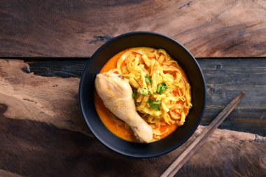 Kuzey Tayland yemekleri (Khao Soi), baharatlı körili şehriye çorbası, tavuklu kase ve ahşap arka planda çubuklar.