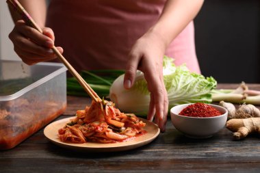 Yemek için ahşap tabakta lahana çubuklarıyla kimchi toplayan kadın, ev yapımı Kore yemeği.