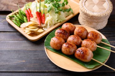 Tayland sosisi veya Isan sosisi (ızgara mayalanmış domuz pirinci) taze lahana, zencefil ve ahşap zemin üzerinde kırmızı biberle yenir.