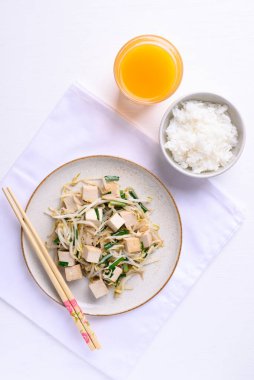 Kızarmış tofuyu mung fasulyesi lahanasıyla karıştırıp beyaz arka planda pilav ve portakal suyuyla yemek, Asya 'nın sağlıklı vejetaryen yemekleri.