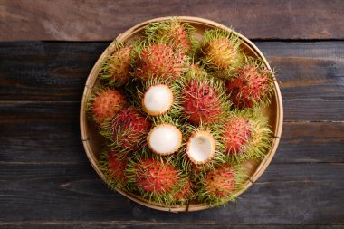 Tahta arka planda bambu sepetinde olgun Rambutan meyvesi, tropik meyve ve yerli Güneydoğu Asya, sulu ve tatlı bir tat.