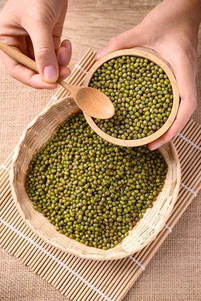 Mung bean seeds in a bowl with spoon holding by hand, Food ingredients in Asian cuisine and produce mung bean sprout