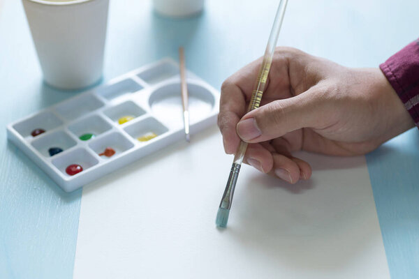 Hand holding brush and painting watercolor on white paper