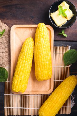 Tahta arka planda bir kasede mısır koçanı ve tereyağı.