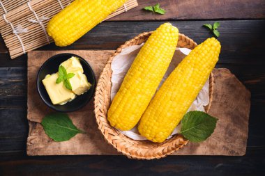 Bambu sepetinde mısır koçanı ve ahşap arka planda bir kasede tereyağı.