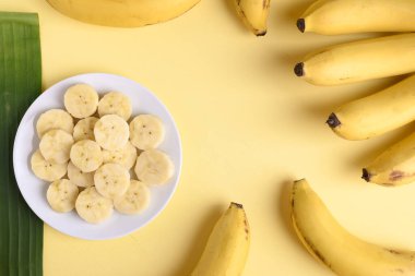 Beyaz tabakta dilimlenmiş muz ve sarı fonda muz meyvesi, tropikal meyve.