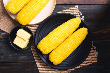 Tahta arka planda bir kasede mısır koçanı ve tereyağı.