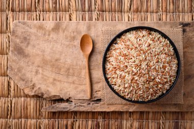 Tahta kaşıklı bir kâse içinde organik Tayland kahverengi pirinç (kargo pilavı, Loonzain pilavı veya kabuklu pirinç), sağlıklı yiyecek, masa üstü görünümü)