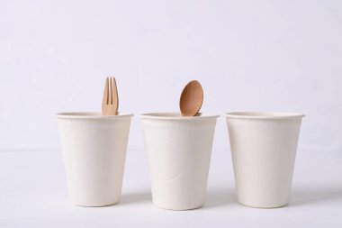 Beyaz zemin üzerinde ahşap çatal ve kaşıkla doğal liften yapılmış biyolojik çözünürlüklü kahve fincanı, çevre dostu ve sürdürülebilirlik kavramı