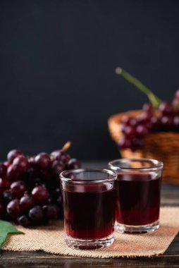 Bardakta kırmızı üzüm suyu, ahşap arka planda taze üzüm, sağlıklı içecek, natürmort.