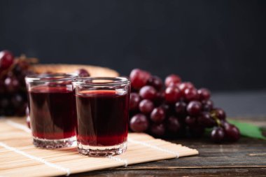 Bardakta kırmızı üzüm suyu, ahşap arka planda taze üzüm, sağlıklı içecek, natürmort.