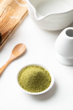 Tahta kaşıklı kibrit yeşil çay tozu, bambu çırpısı ve beyaz arka planda Chawan kasesi.