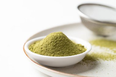 Matcha green tea powder in bowl and sieve on plate with white background