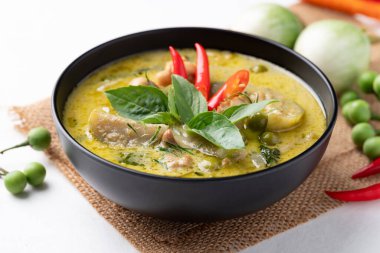 Thai green curry chicken in black bowl with ingredients on white background