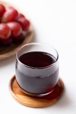 Bardakta kırmızı üzüm suyu ve beyaz arka planda taze üzüm meyvesi, sağlıklı içecek.