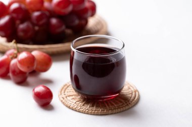 Bardakta kırmızı üzüm suyu ve beyaz arka planda taze üzüm meyvesi, sağlıklı içecek.