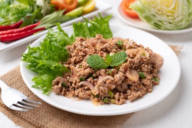 Yerel Tayland yemekleri, baharatlı domuz salatası (Larb Moo) beyaz arka planda taze sebzelerle yemek