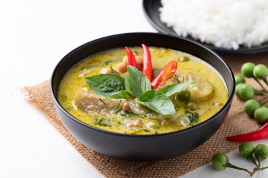 Tayland yeşil körili tavuğu siyah kasede pilav ve malzemeler beyaz arka planda.