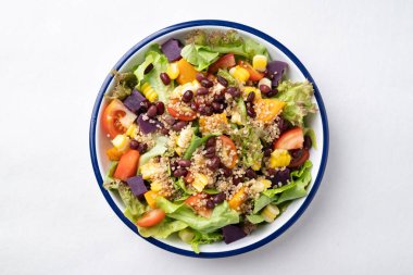 Marullu sağlıklı sebze salatası, kinoa tohumu, azuki fasulyesi, mısır, domates, balkabağı ve mor patatesli beyaz arka planda bir kasede. Vejetaryen ve bitkisel gıda