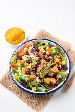 Marullu sağlıklı sebze salatası, kinoa tohumu, azuki fasulyesi, mısır, domates, kabak kabağı ve mor tatlı patates ve beyaz arka planda kabak sosu. Vejetaryen ve bitkisel gıda
