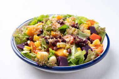 Marullu sağlıklı sebze salatası, kinoa tohumu, azuki fasulyesi, mısır, domates, balkabağı ve mor patatesli beyaz arka planda bir kasede. Vejetaryen ve bitkisel gıda