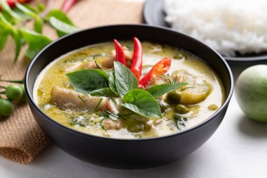 Tayland yeşil körili tavuğu siyah kasede pilav ve malzemeler beyaz arka planda.