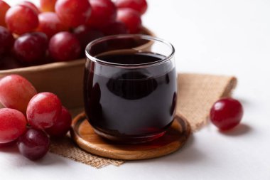 Bardakta kırmızı üzüm suyu ve beyaz arka planda taze üzüm meyvesi, sağlıklı içecek.