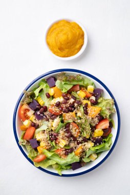 Marullu sağlıklı sebze salatası, kinoa tohumu, azuki fasulyesi, mısır, domates, kabak kabağı ve mor tatlı patates ve beyaz arka planda kabak sosu. Vejetaryen ve bitkisel gıda