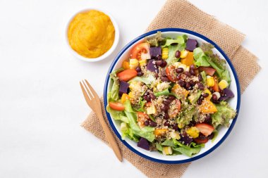 Marullu sağlıklı sebze salatası, kinoa tohumu, azuki fasulyesi, mısır, domates, kabak kabağı ve mor tatlı patates ve beyaz arka planda kabak sosu. Vejetaryen ve bitkisel gıda