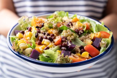 Marullu sağlıklı sebze salatası, kinoa tohumu, azuki fasulyesi, mısır, domates, balkabağı ve kadın eli tarafından tutulan mor tatlı patates. Vejetaryen ve bitkisel gıda