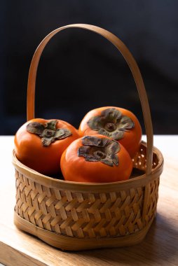 Tahta arka planda sepetteki olgun hurma meyvesi, sonbahar meyvesi