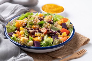 Marullu sağlıklı sebze salatası, kinoa tohumu, azuki fasulyesi, mısır, domates, kabak kabağı ve mor tatlı patates ve beyaz arka planda kabak sosu. Vejetaryen ve bitkisel gıda