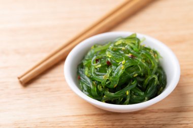 Tahta zemin üzerinde çubuklar olan bir kasede susam tohumlu yosun salatası