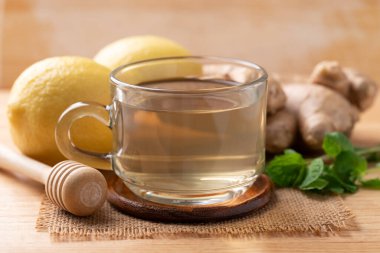 Ahşap zemin üzerinde bardakta limon ve zencefil çayı, sağlıklı sıcak içecek.