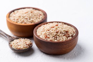 Tahta kase ve beyaz arka planda kaşık içinde Tayland kahverengi pirinç tohumu (İskoç yabani pirinci)