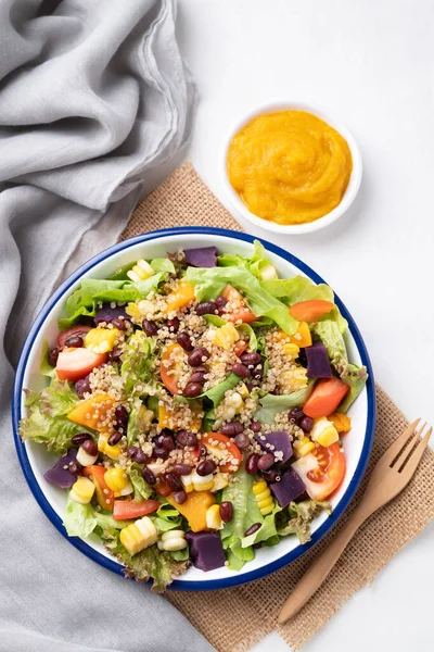 Marullu sağlıklı sebze salatası, kinoa tohumu, azuki fasulyesi, mısır, domates, kabak kabağı ve mor tatlı patates ve beyaz arka planda kabak sosu. Vejetaryen ve bitkisel gıda