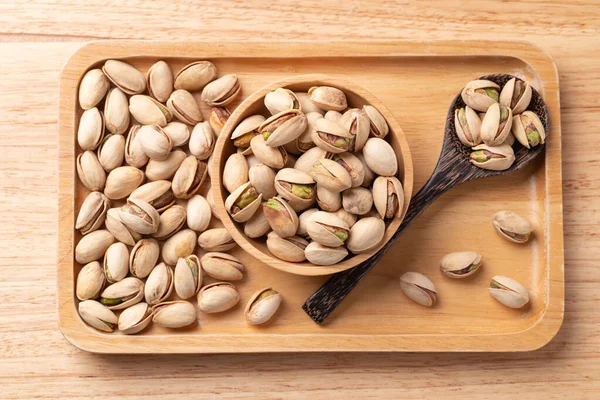 Ahşap tabakta kaşıkla kase içinde kavrulmuş fıstık, masa üstü manzaralı.
